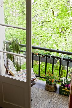 an open door leading to a balcony with potted plants on the floor and trees in the background