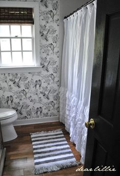 a bathroom with black and white wallpaper, striped rug, toilet and shower curtain