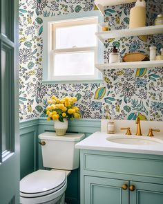 a white toilet sitting next to a sink in a bathroom under a window with yellow flowers on it