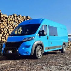 a blue van parked next to a pile of logs