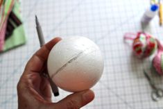 a person holding an egg in their hand with scissors and other crafting supplies on the table