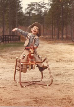 a young boy riding on top of a wooden toy horse in the middle of a dirt road