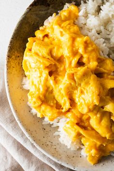 a white plate topped with rice covered in yellow sauce next to a fork and spoon