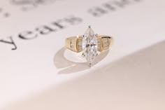 a yellow gold ring with a pear shaped diamond in the center on top of a piece of paper