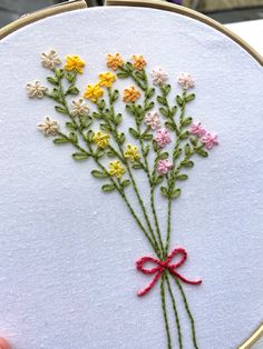 a hand embroidered flower bouquet on a white piece of fabric with a red ribbon in the center