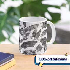 a coffee mug with bats on it sitting on a table next to some books and a plant