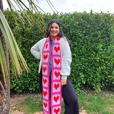 a woman standing in front of a hedge wearing a pink scarf with hearts on it