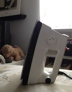 a computer monitor sitting on top of a bed next to a teddy bear in front of a window