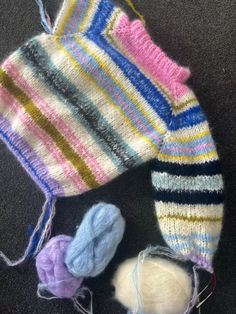 two knitted mittens, one with yarn and the other with wool balls on it