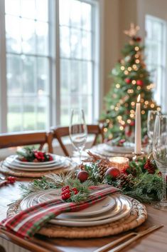 a dining room table set for christmas with plates and place settings in front of the tree