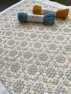 two skeins of yarn sitting on top of a quilted tablecloth with yellow and blue designs