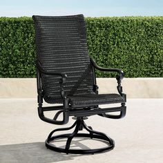 a black patio chair sitting on top of a cement floor next to a hedge covered wall