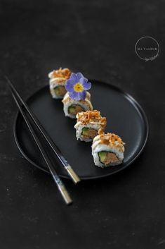 a black plate topped with sushi next to chopsticks and a purple flower