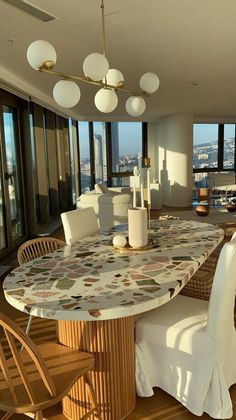 a dining room table with white chairs and large windows overlooking the cityscape in the background