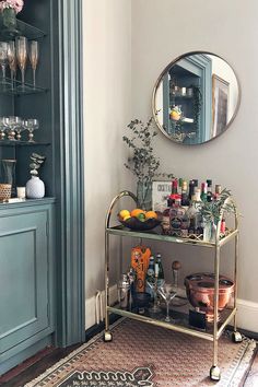 a bar cart with drinks on it in front of a mirror and blue cupboards