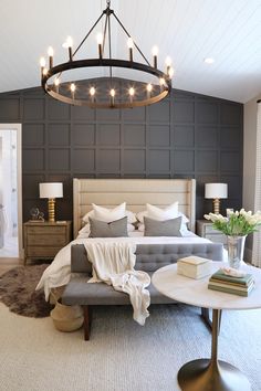 a large bed sitting under a chandelier next to a table with books on it