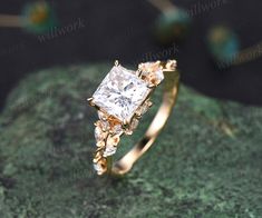 a gold ring with a princess cut diamond in the center on top of a green rock