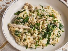 a white bowl filled with pasta and spinach on top of a patterned table cloth