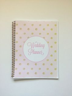 a pink and gold wedding planner on a white wall with polka dot paper in the middle