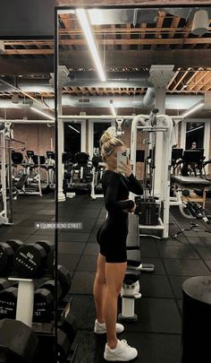 a woman standing in front of a mirror at a gym