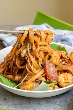 a white bowl filled with noodles and shrimp on top of a table next to a fork