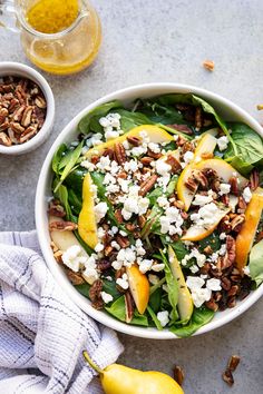 a white bowl filled with spinach salad next to two bowls of fruit and nuts