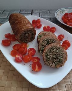 some food is on a white plate with tomatoes and meatloaf roll slices next to it