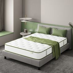 a white bed with green sheets and pillows in a room next to a lamp on the wall