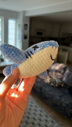 a hand is holding a small toy shark in the middle of a living room area