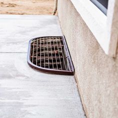 a grate on the side of a building next to a window with bars in it