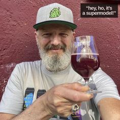 a man holding a glass of wine in front of a red wall