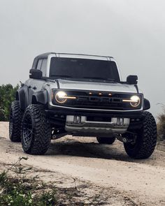 the front end of a gray truck on a dirt road with trees in the background