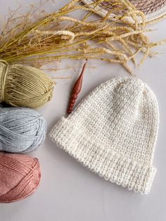 three skeins of yarn next to a crochet hat and knitting needles