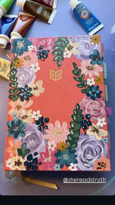 an open book with flowers on it sitting on a table next to some pens and pencils