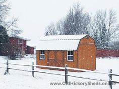 a small red barn in the middle of a snowy day with trees and fence around it