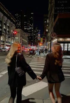 two women holding hands while crossing the street at night in new york city, usa