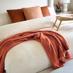 a white bed with orange pillows and blankets on it's headboard in a bedroom