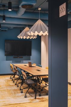 an empty conference room with blue walls and wooden tables, chairs, and a flat screen tv