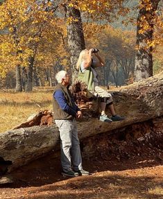 an older man and young boy are sitting on a fallen tree in the woods, looking at each other