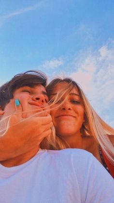 two people taking a selfie in front of a blue sky with clouds behind them