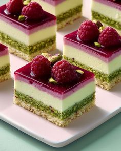 four pieces of cake with raspberries and pistachio toppings on a plate