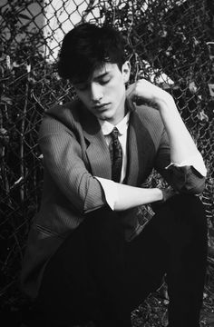 black and white photograph of a young man leaning against a fence with his hands on his hips