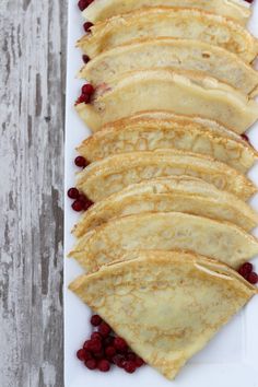 crepes with raspberries are arranged on a white platter, ready to be eaten