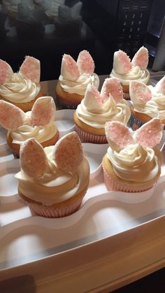 cupcakes with white frosting and pink bows on top are sitting on a tray