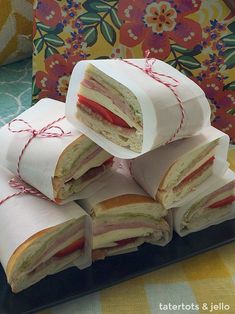 several sandwiches wrapped in white paper on a black plate next to a colorful wallpaper