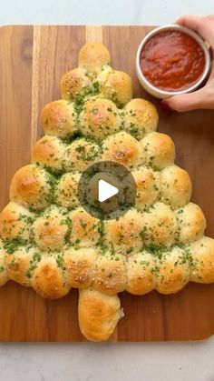 a christmas tree made out of rolls on a cutting board with sauce in the background