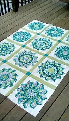 a quilted table runner on a deck with blue and green flowers in the center