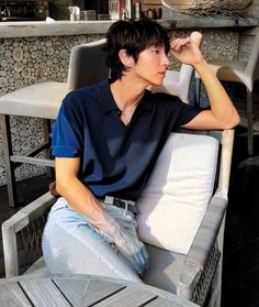 a young man sitting on top of a wooden bench next to a table with chairs