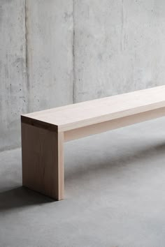 a wooden bench sitting on top of a cement floor in front of a concrete wall