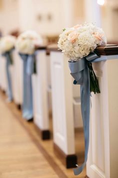 a row of white and blue pews with flowers on the top, tied to them